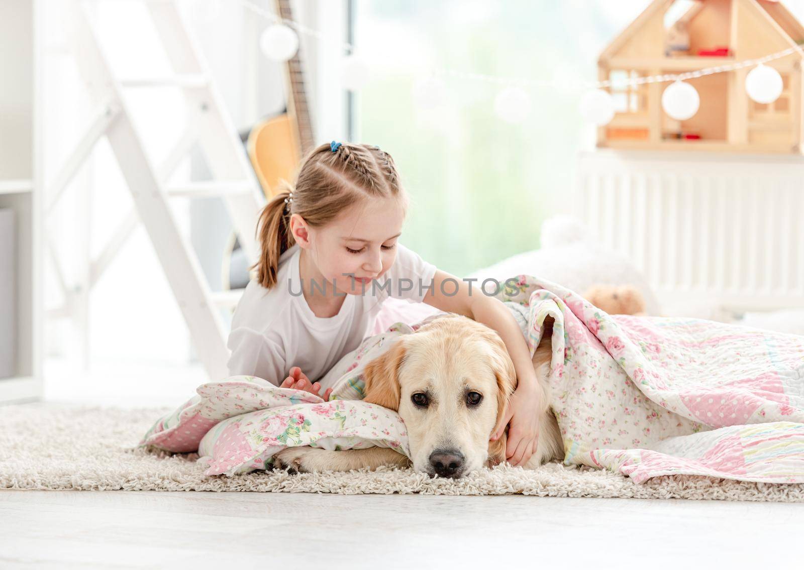 Beautiful little girl covering cute dog with blanket on floor in playroom