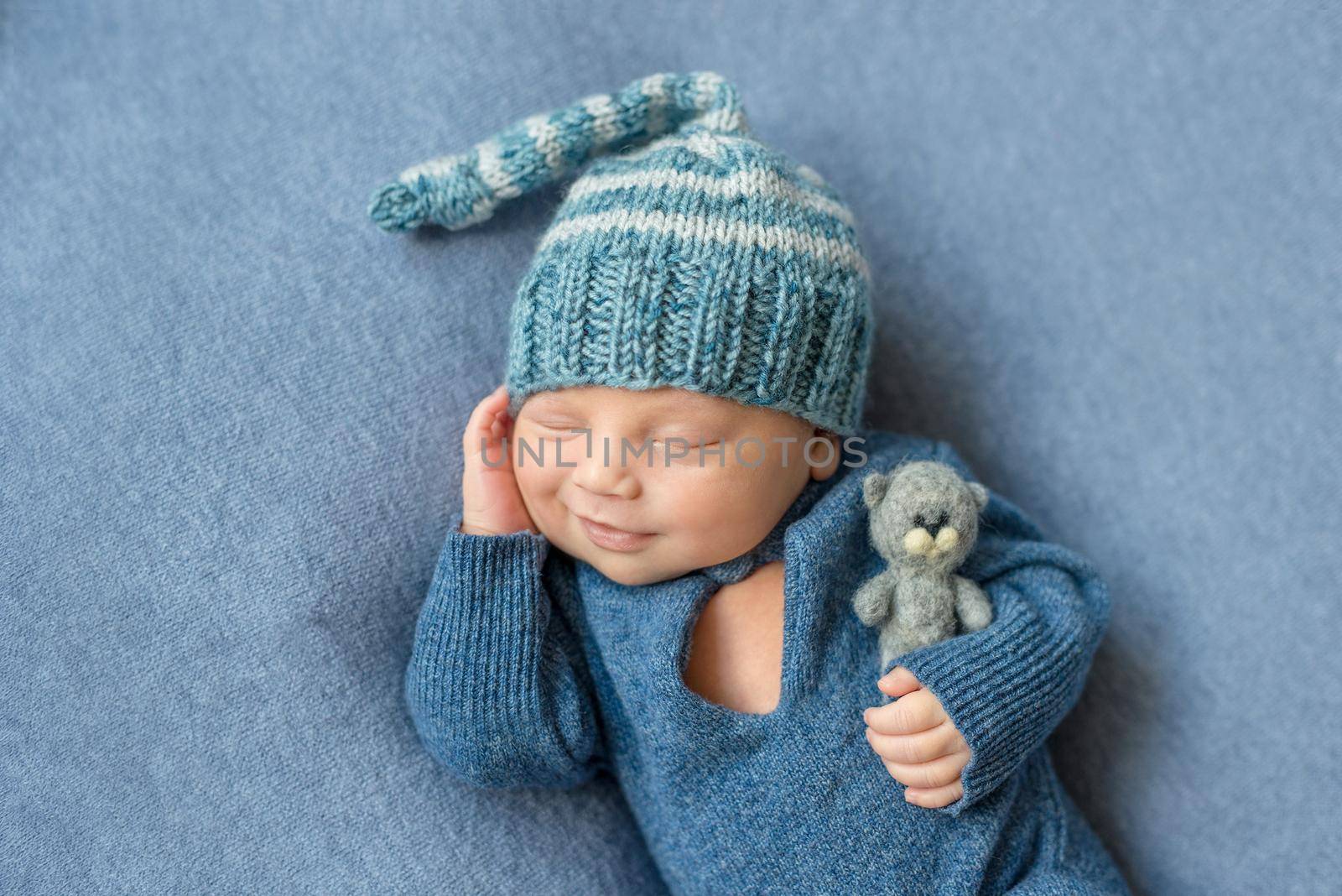 smilimg sleeping newborn in blue suit and hat with toy by tan4ikk1