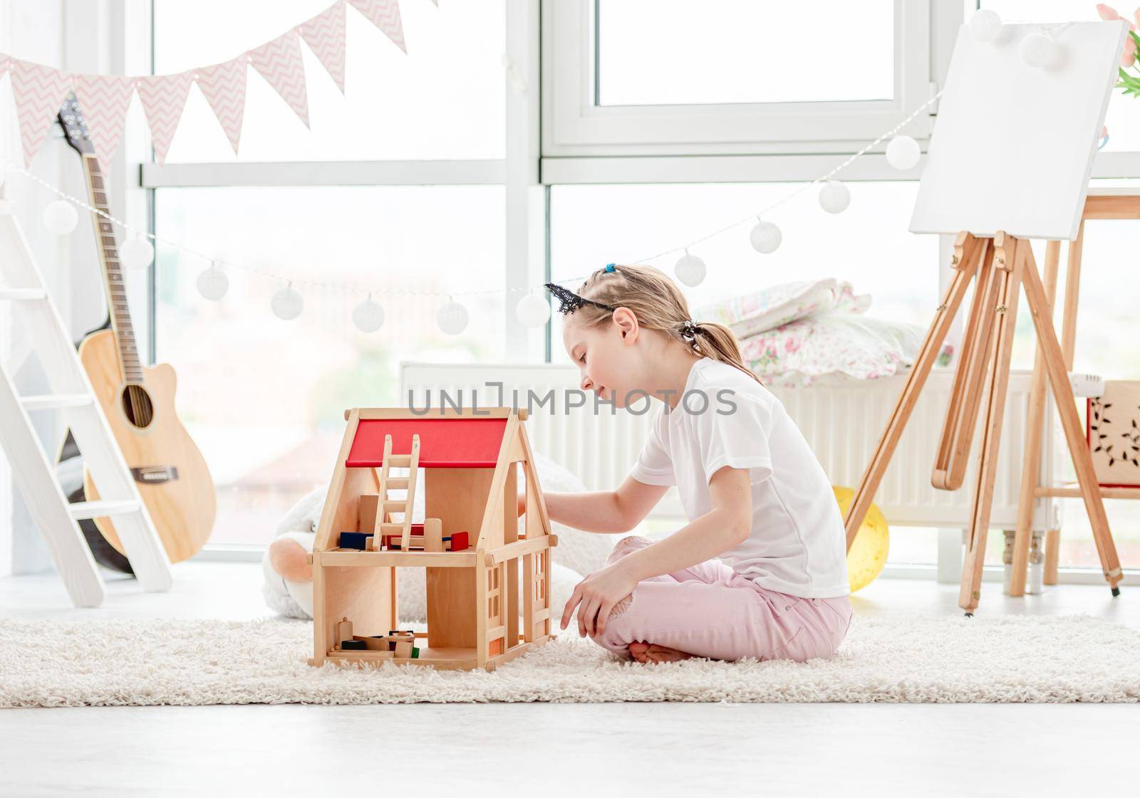 Pretty little girl plays with wooden dollhouse in children's room