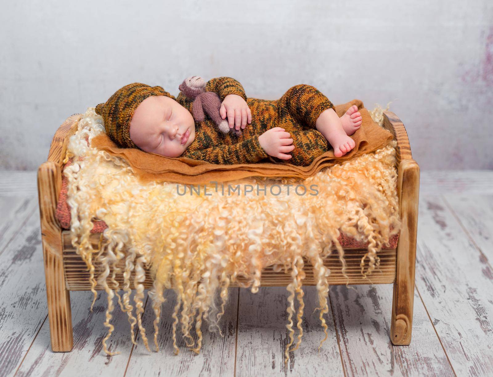 sleeping newborn boy in hat and suit on little bed with fluffy blanket