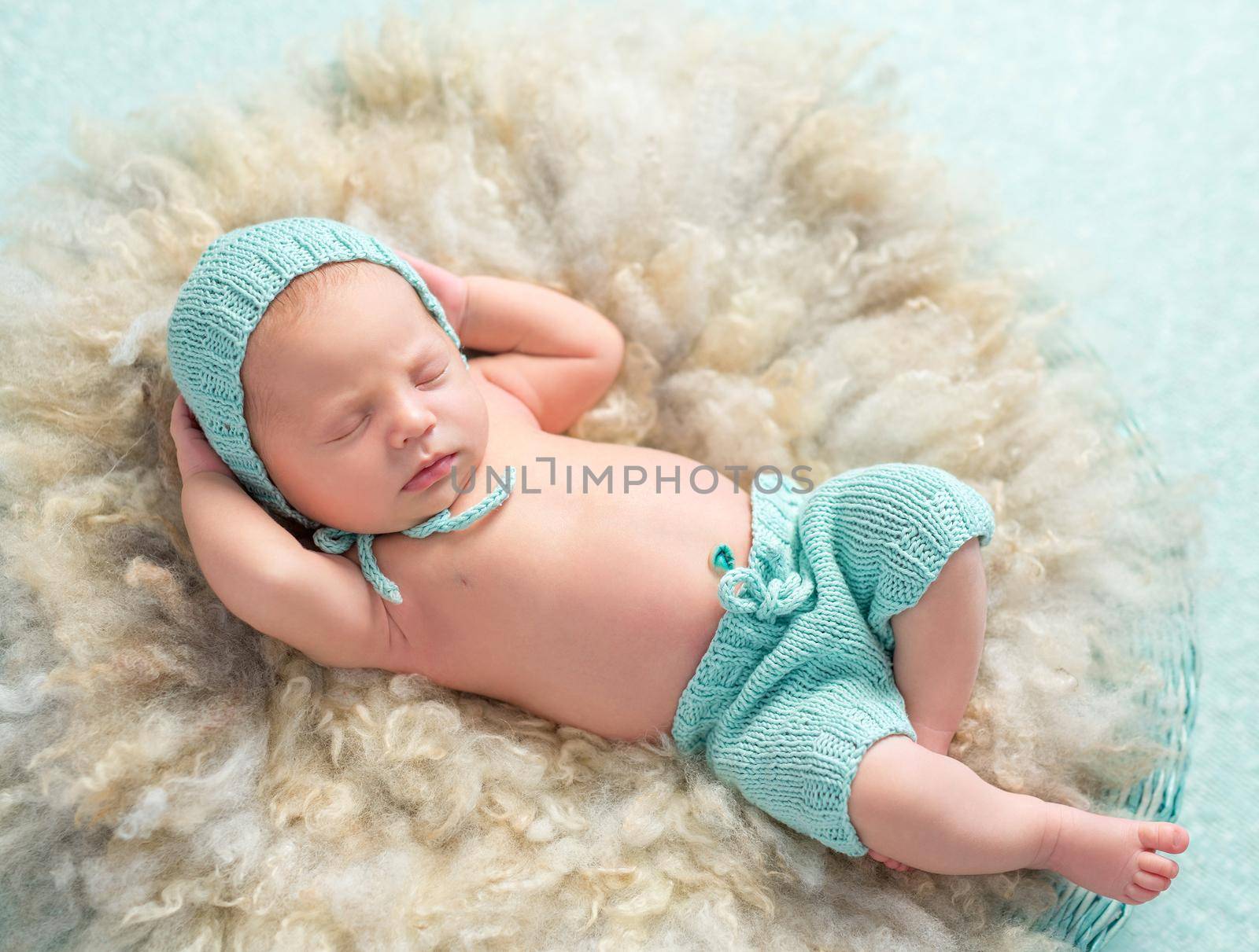 funny newborn boy sleeping with hands behind his head on round fluffy bed