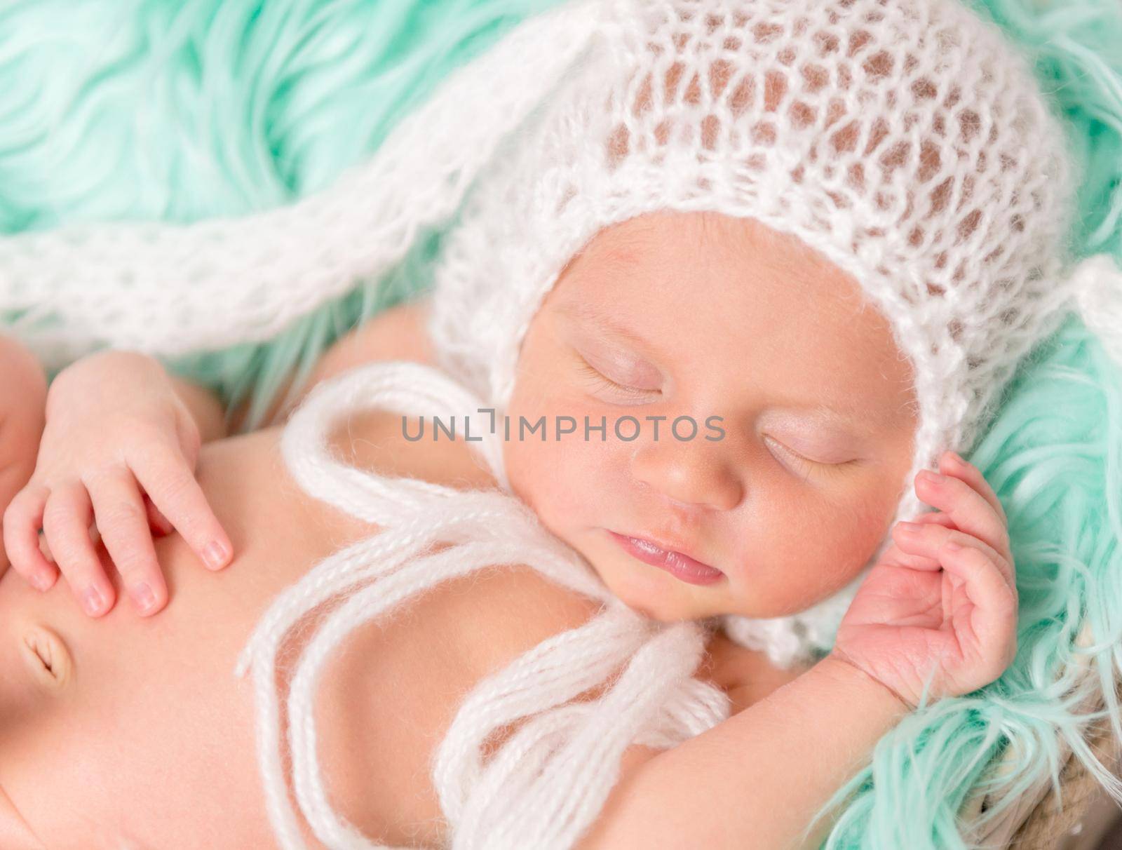 lovely newborn baby in hat sleeping on turquoise fluffy blanket, closeup
