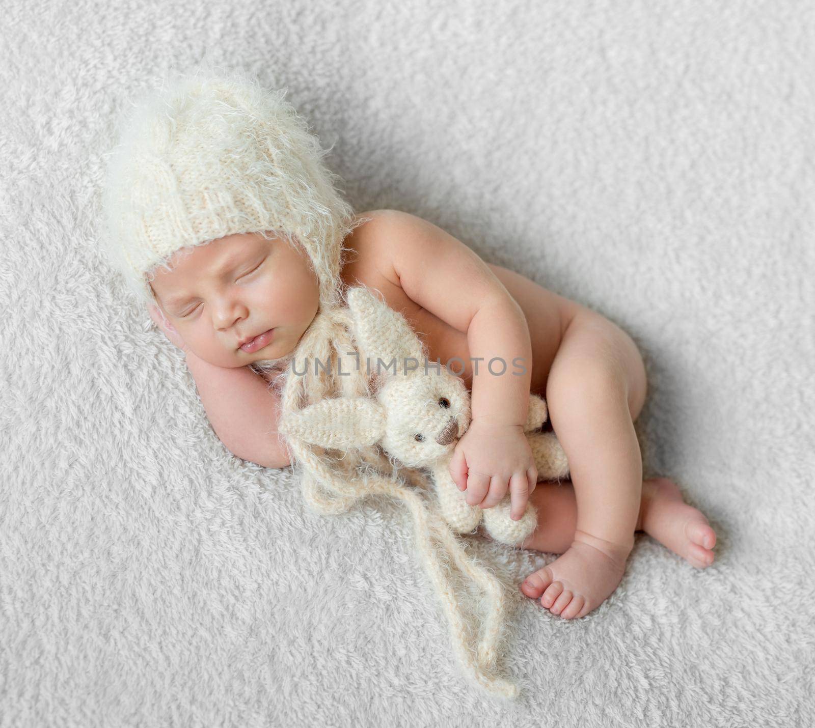 bare sleeping baby in hat with toy on white blanket by tan4ikk1