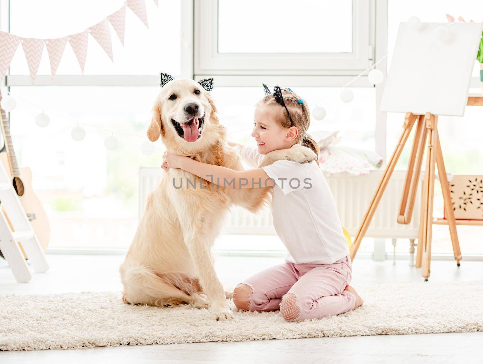 Cheerful little girl having fun with cute dog in playroom