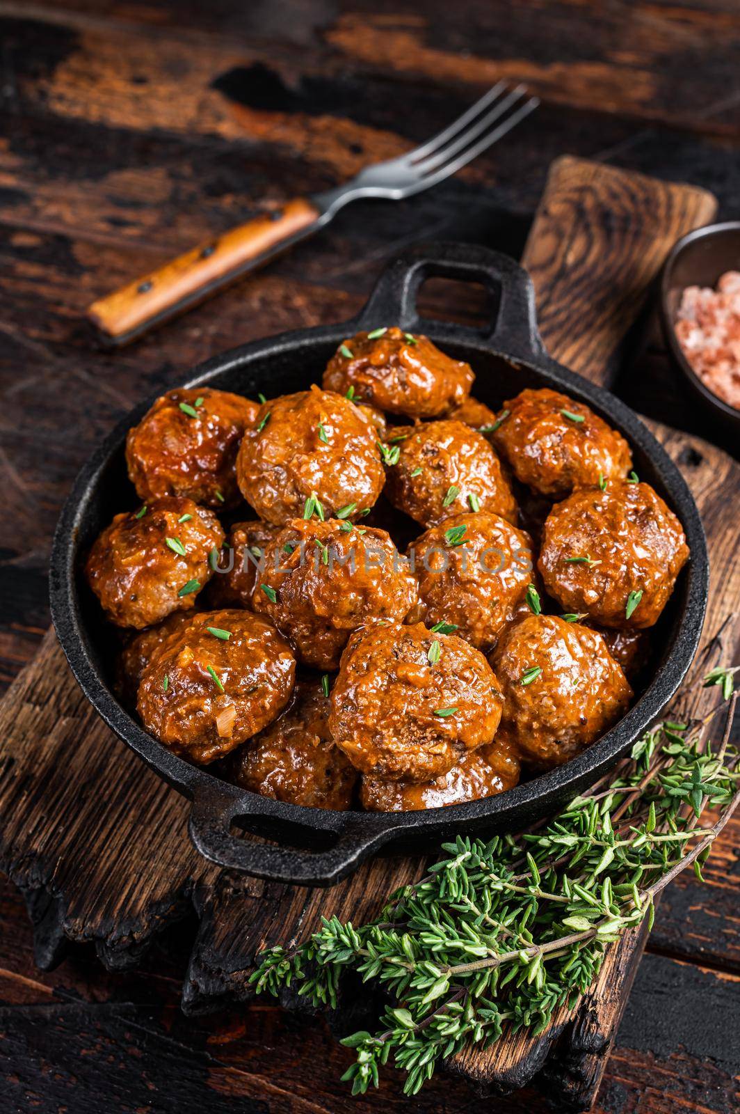 Meatballs in tomato sauce from beef and pork meat with thyme in rustic pan. Dark background. Top view.