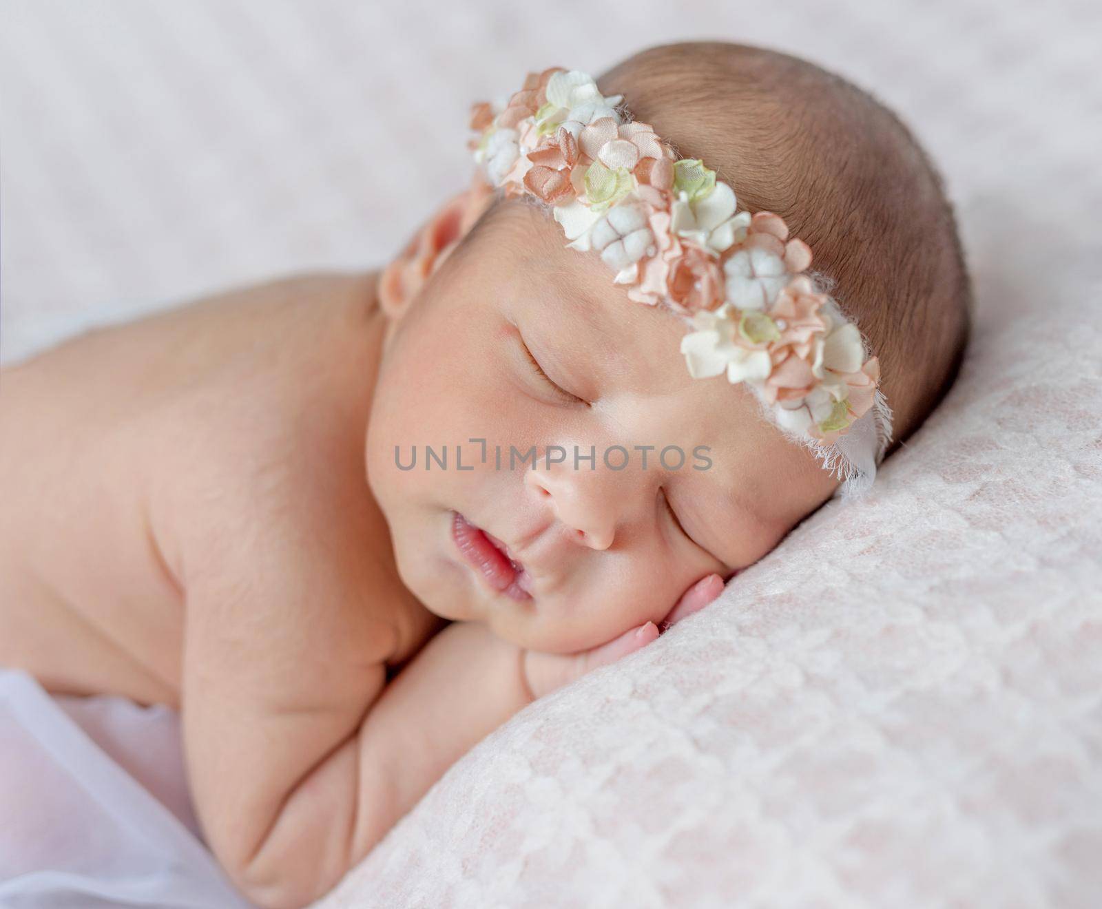 funny sleeping newborn girl with her hands under her head and headband with flowers