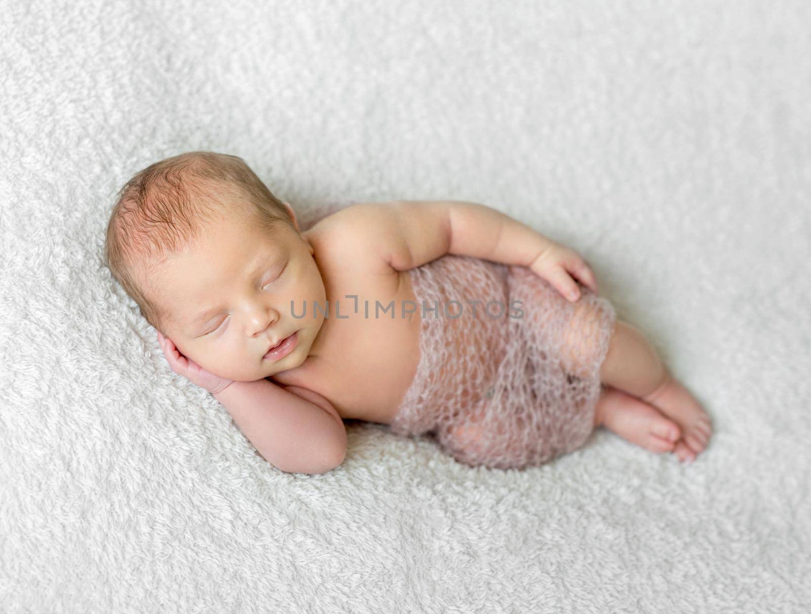 lovely smiling sleeping baby covered with light knitted shawl on white blanket