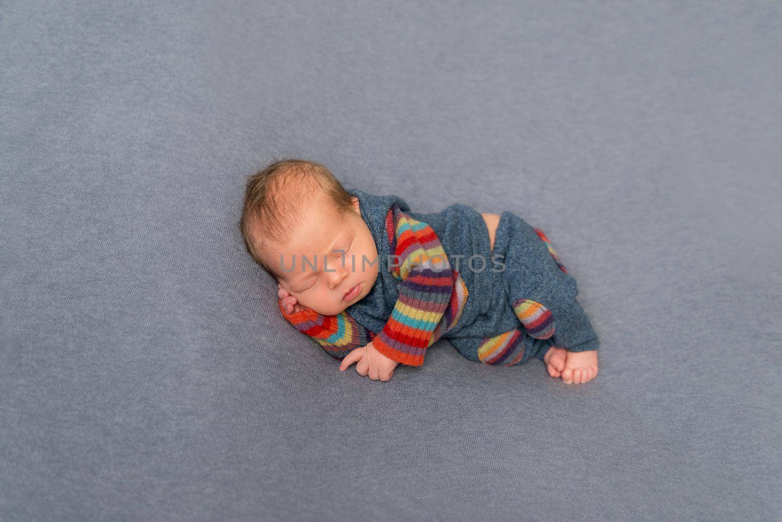 Sweet hairy newborn napping on his side, in striped pants and jacket