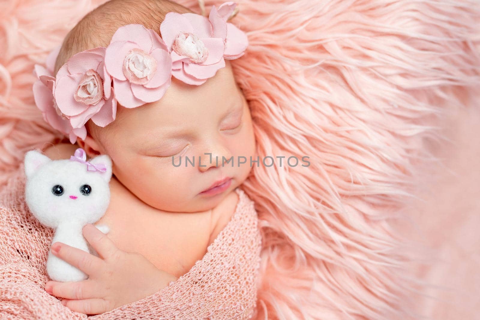 lovely sleeping newborn girl holding toy on pink fluffy blanket