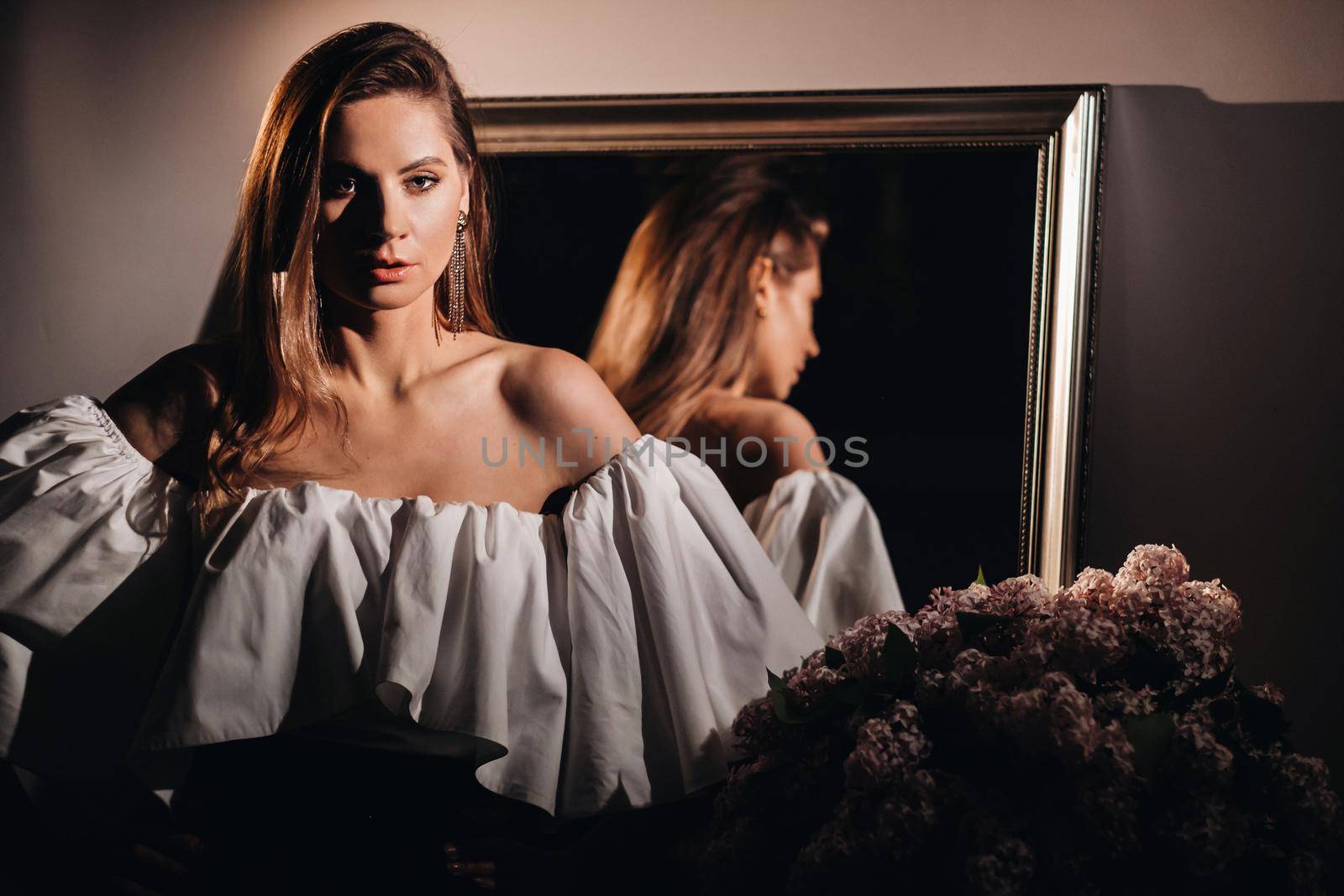Beautiful girl in the mirror reflection at home. Girl before the holiday near the home mirror.A girl in a white dress with long hair is going to a party at home by Lobachad