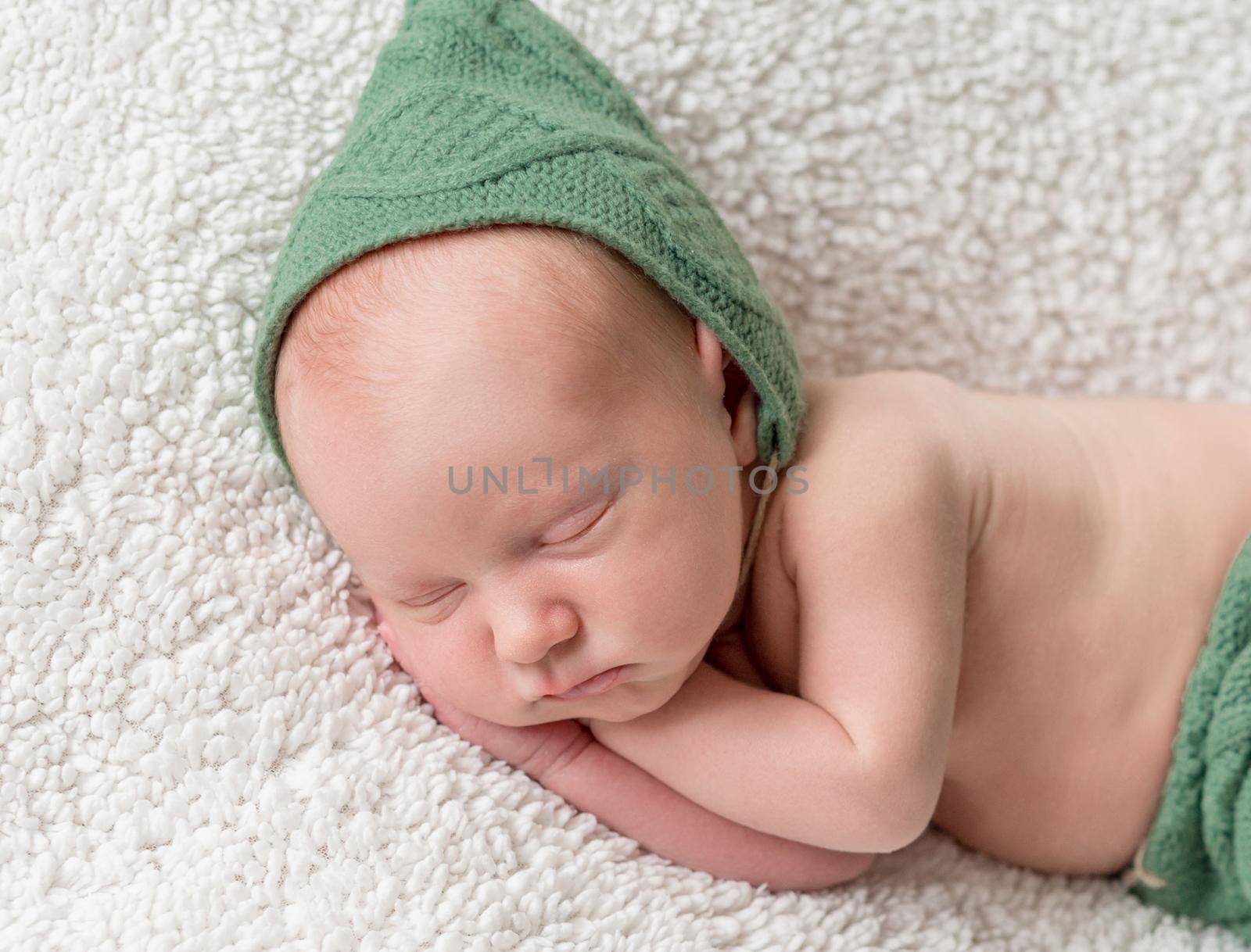 cute newborn sleeping in green elf hat and panties on soft white blanket close-up