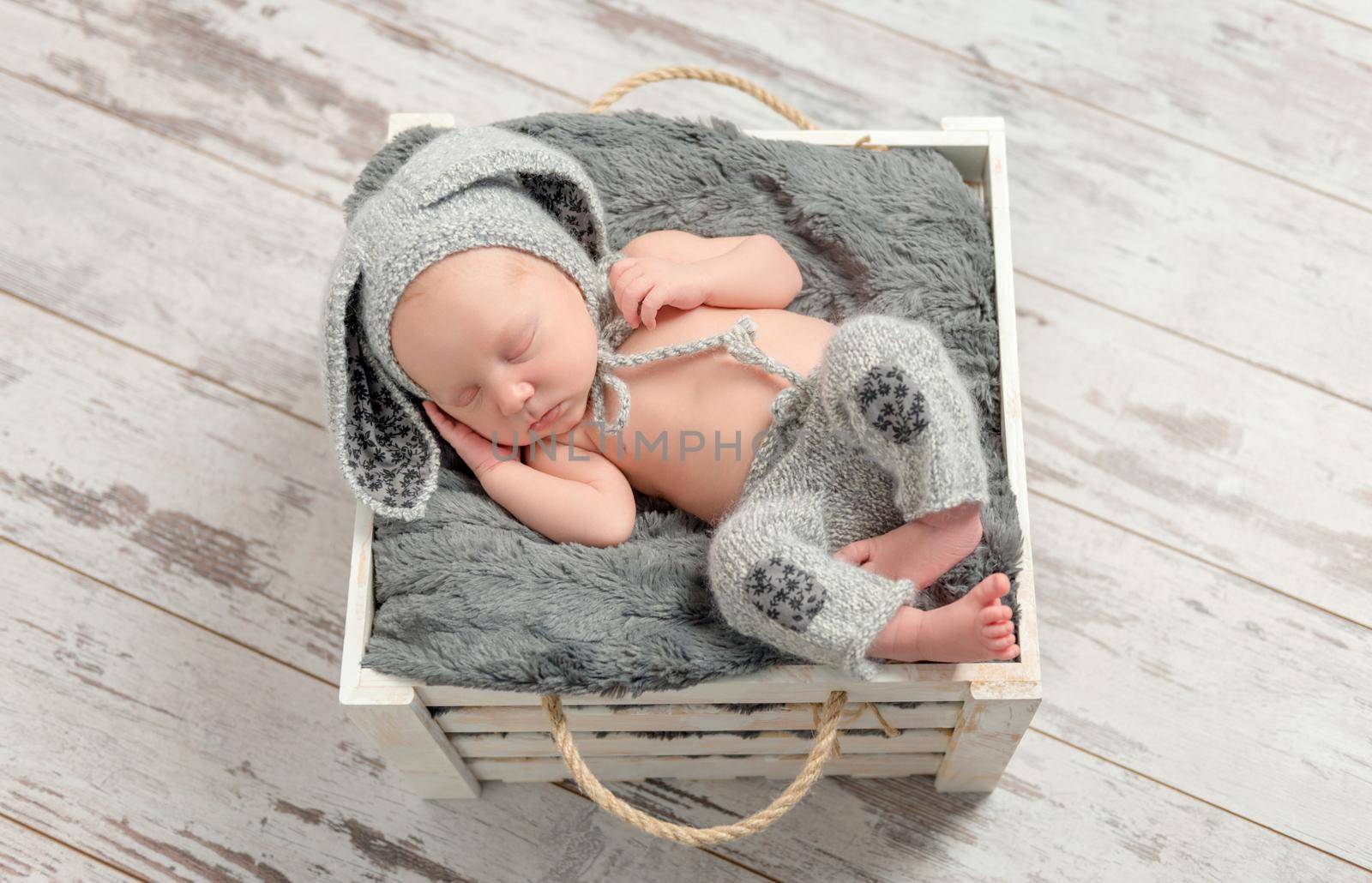 sweet sleeping baby in gray panties and hat with hare ears with toy on basket, top view