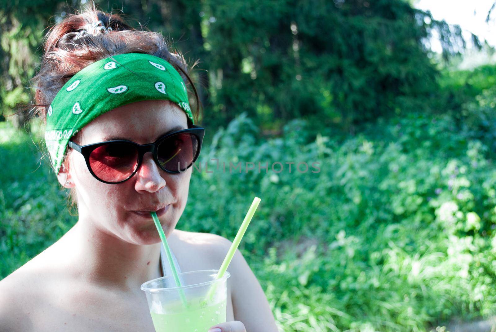 Young beautiful girl drinking a green drink from a plastic cup takeaway food. Summer cold drinks.