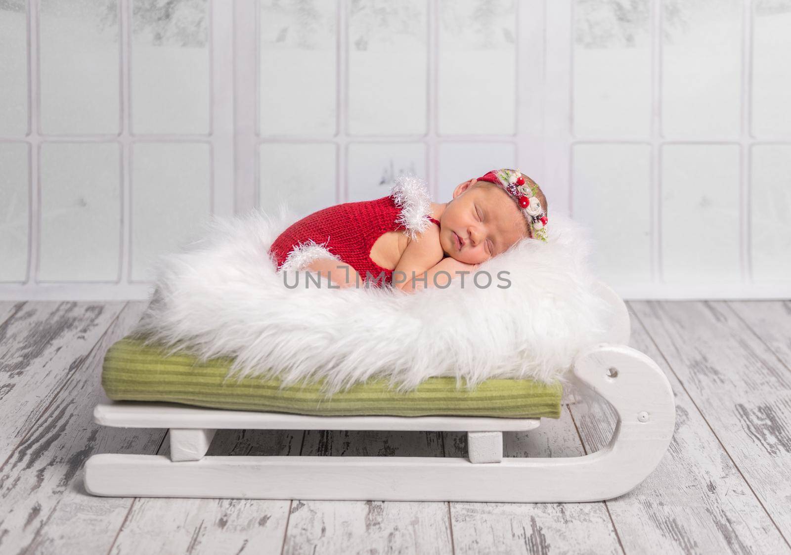 beautiful newborn in red romper sleeping on sleigh cot with white fluffy blanket