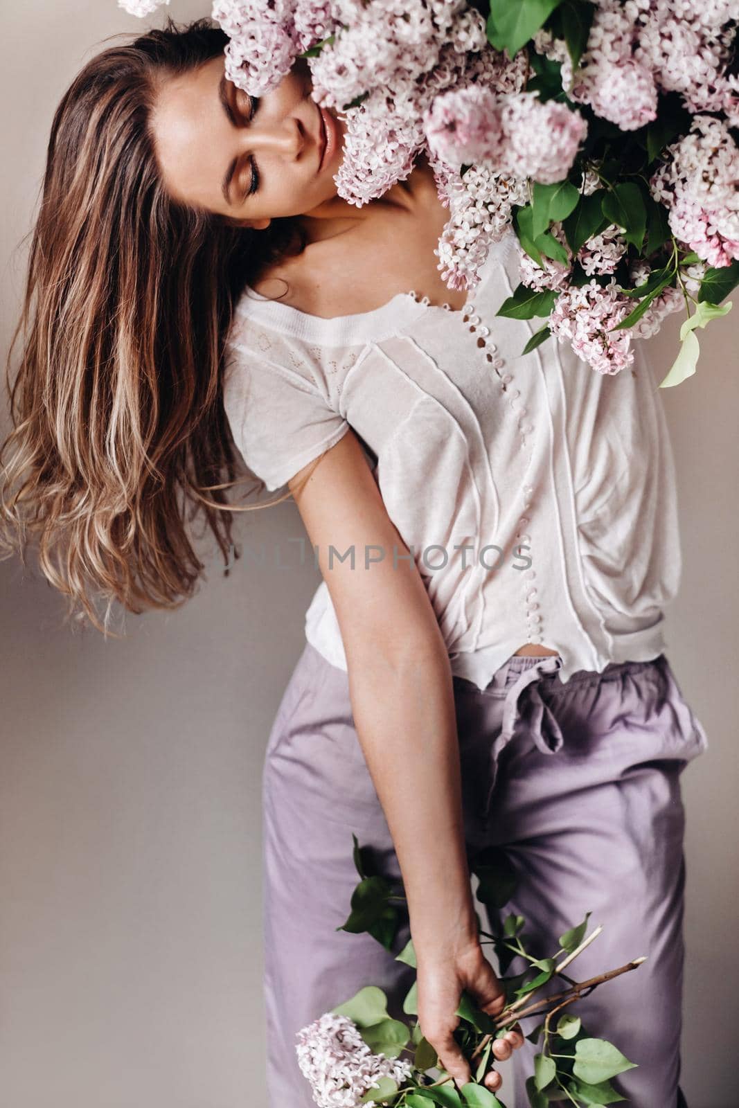 Beautiful girl with lilac flowers in her hands. A girl with lilac flowers in the spring at home. A girl with long hair and lilac in her hands.