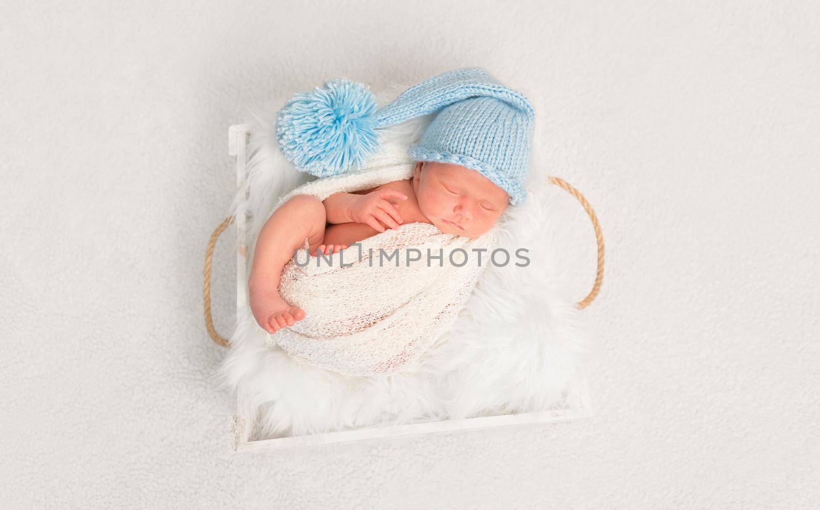 Sweet infant in a blue hat resting with his foot out of a covering blanket