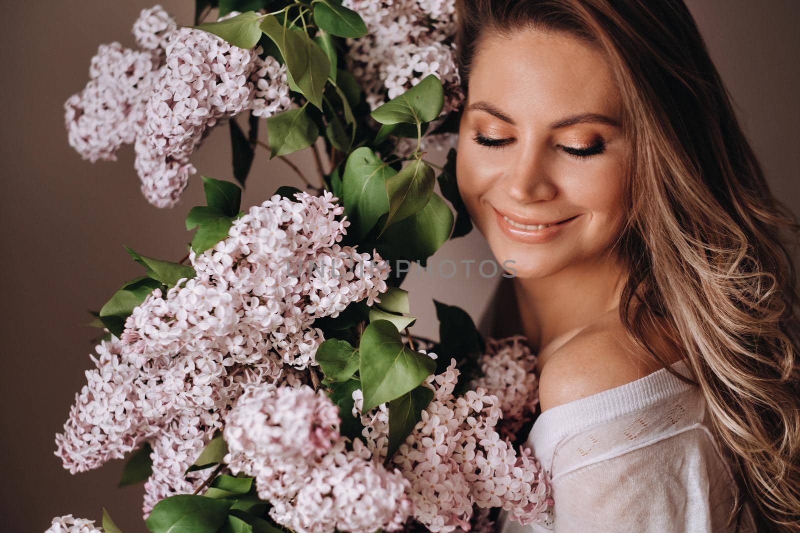 Beautiful girl with lilac flowers in her hands. A girl with lilac flowers in the spring at home. A girl with long hair and lilac in her hands.