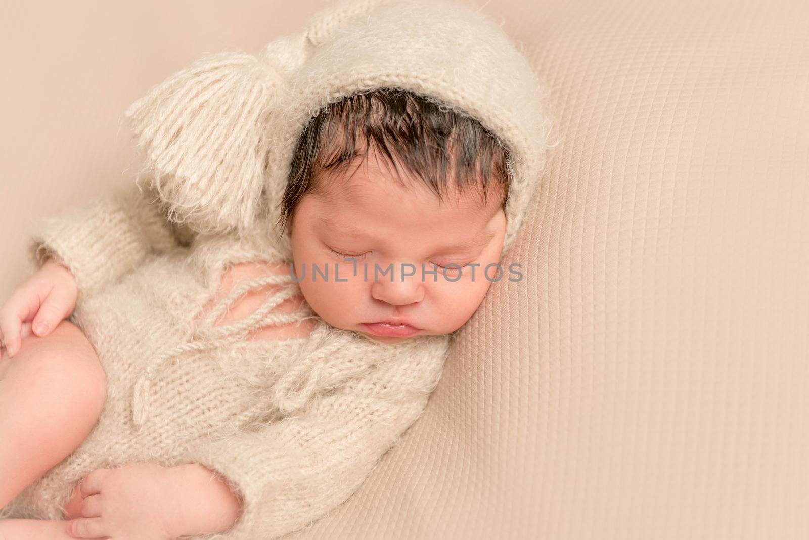 Adorable baby sleeping in a soft yellowish outfit, on a soft surface, on his side