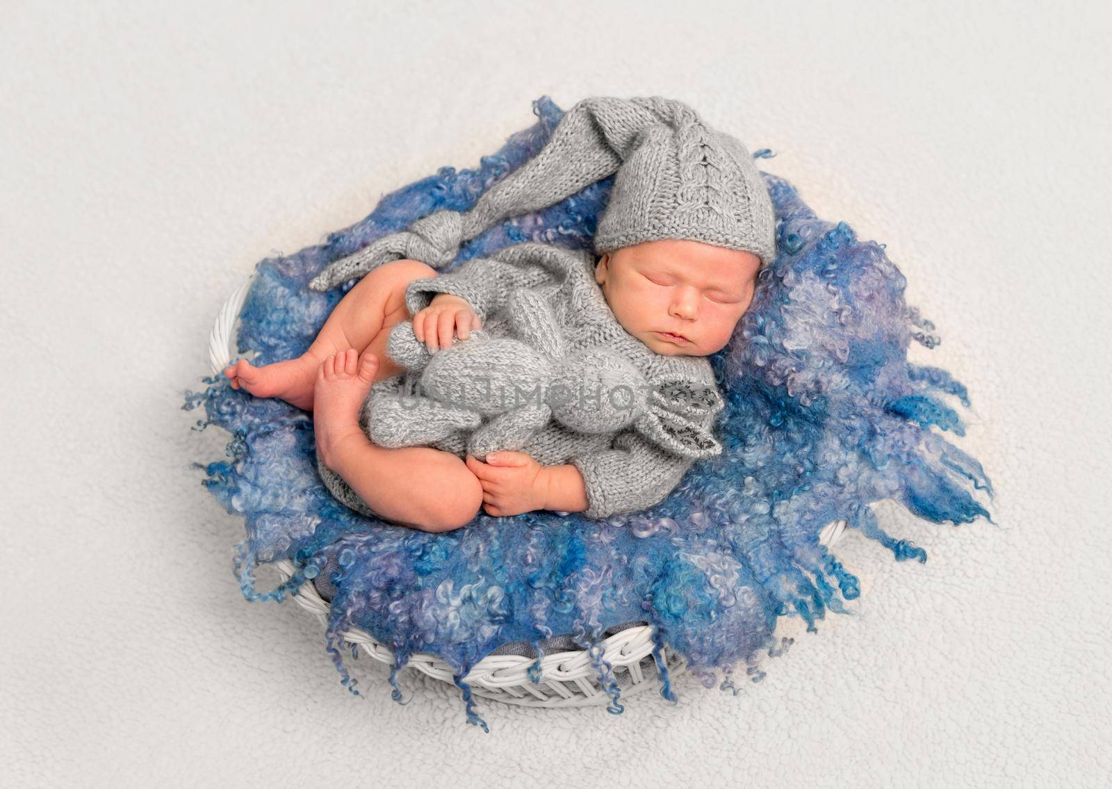 Infant in cute grey knitted outfit sleeping with his favorite toy on a fluffy pillow