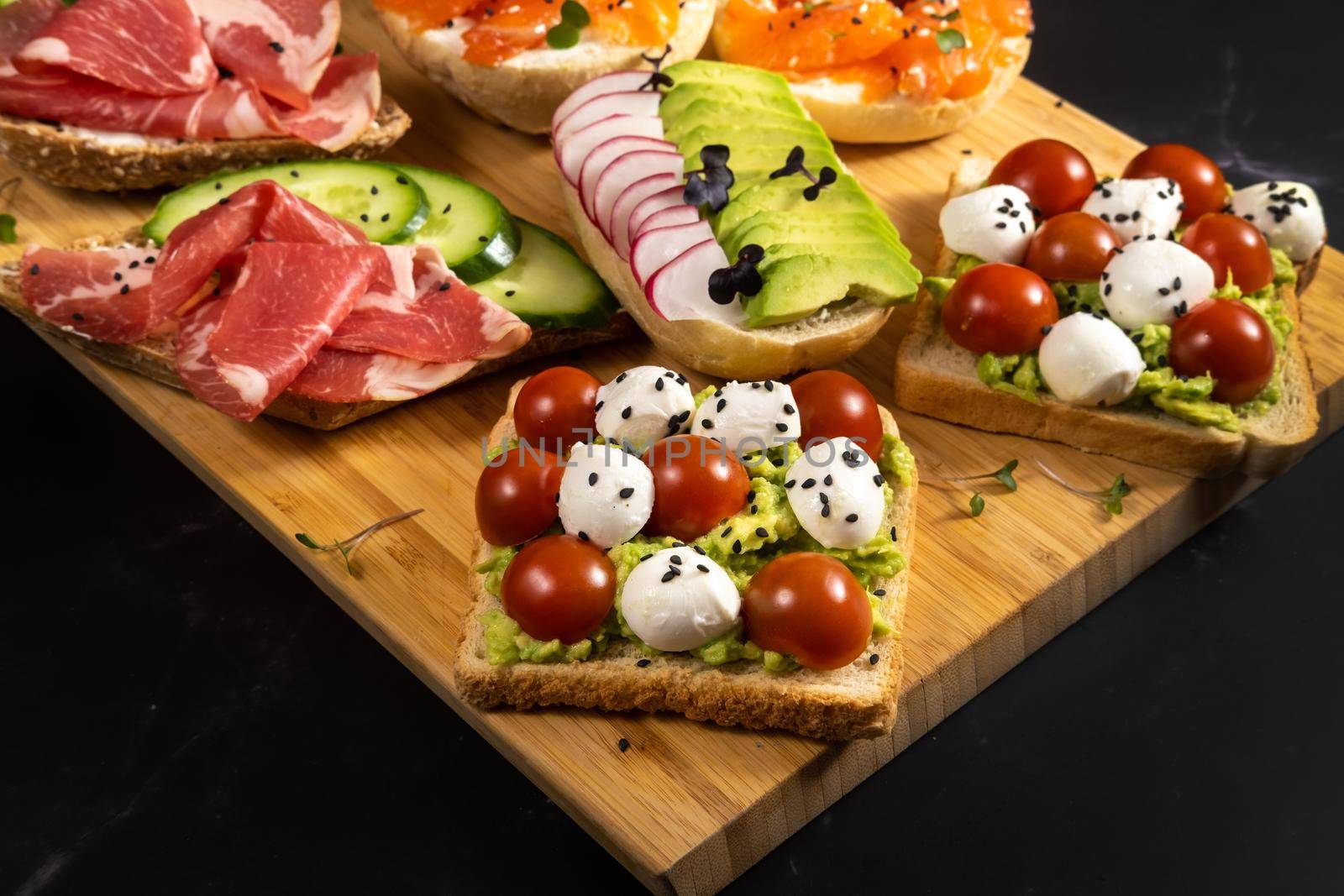 An assortment of sandwiches with fish, cheese, meat and vegetables lay on the board and a bun.