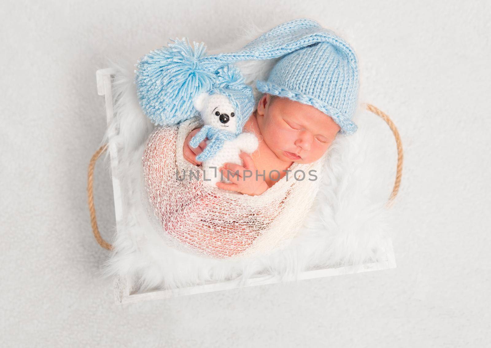 Sleeping kid in enourmous knitted hat holding a teddy, wrapped in a blanket, topview