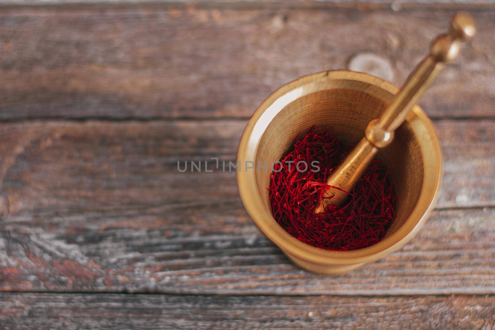 Raw organic red dried saffron spice on wooden background in vintage metal brass mortar with pestle.