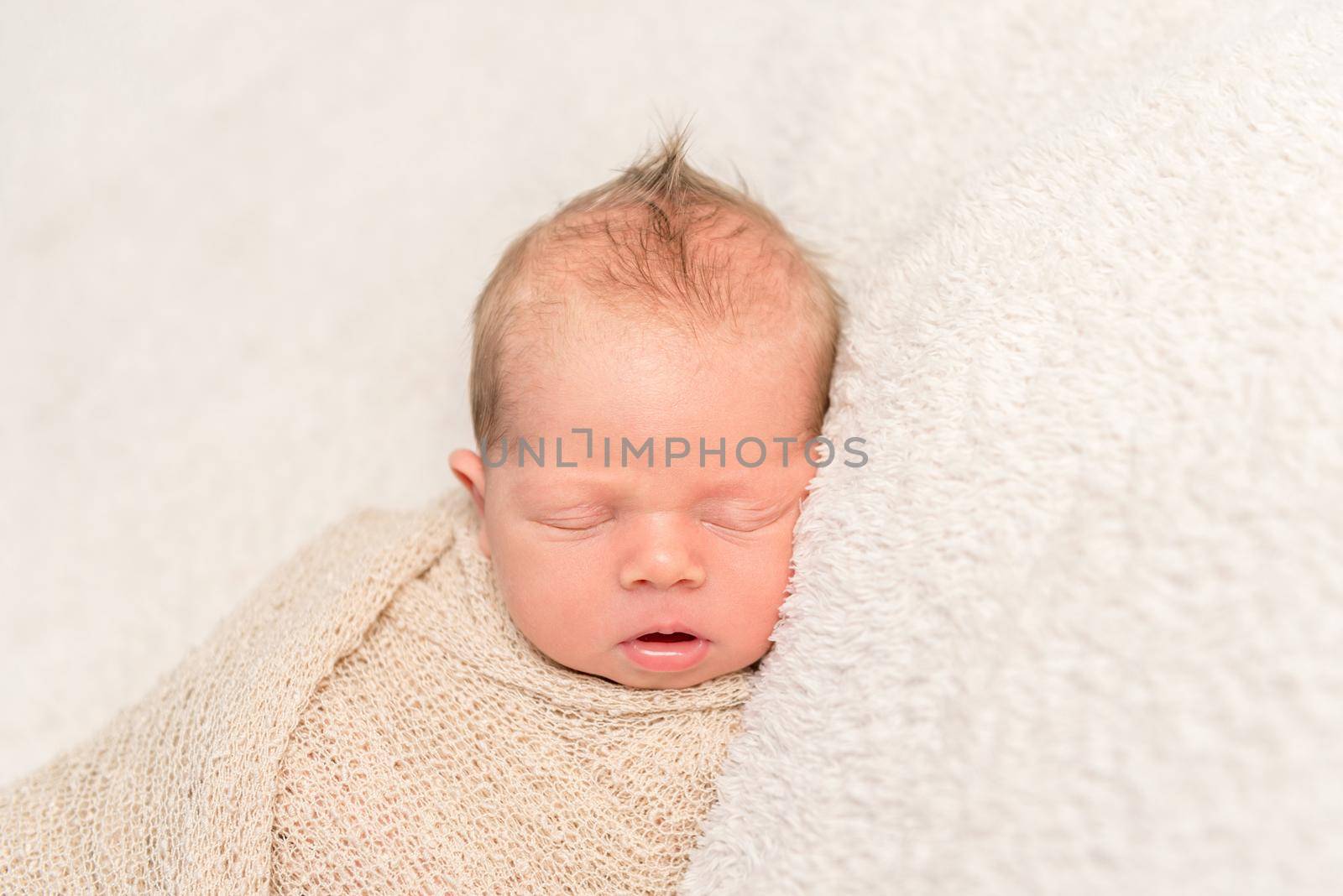 Tiny infant with cute mimic napping after a tought day, swaddled in a blanket