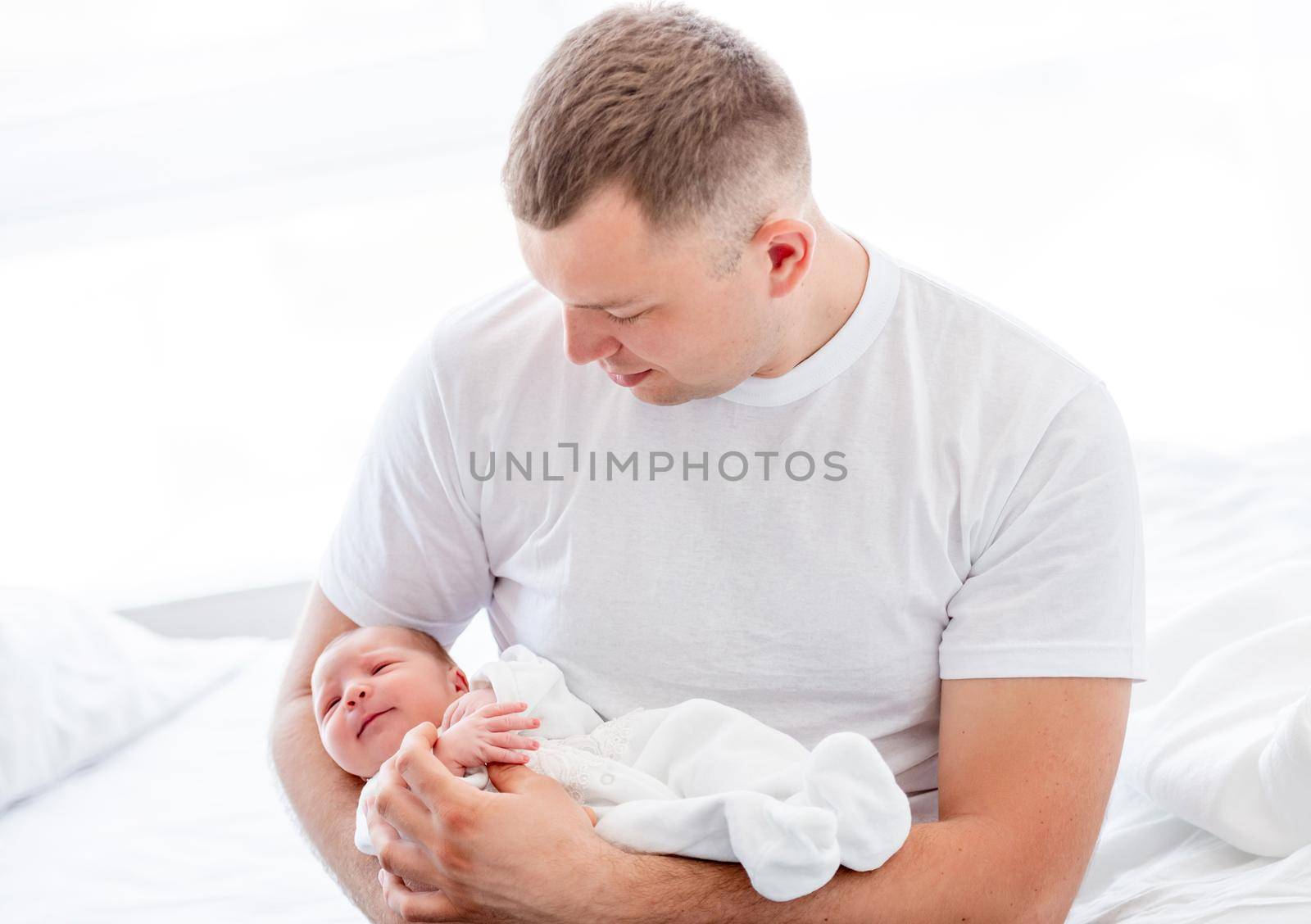 Adorable newborn baby girl wearing white costume sleeping in father hands. Cute infant child napping at home and parent dad holding her