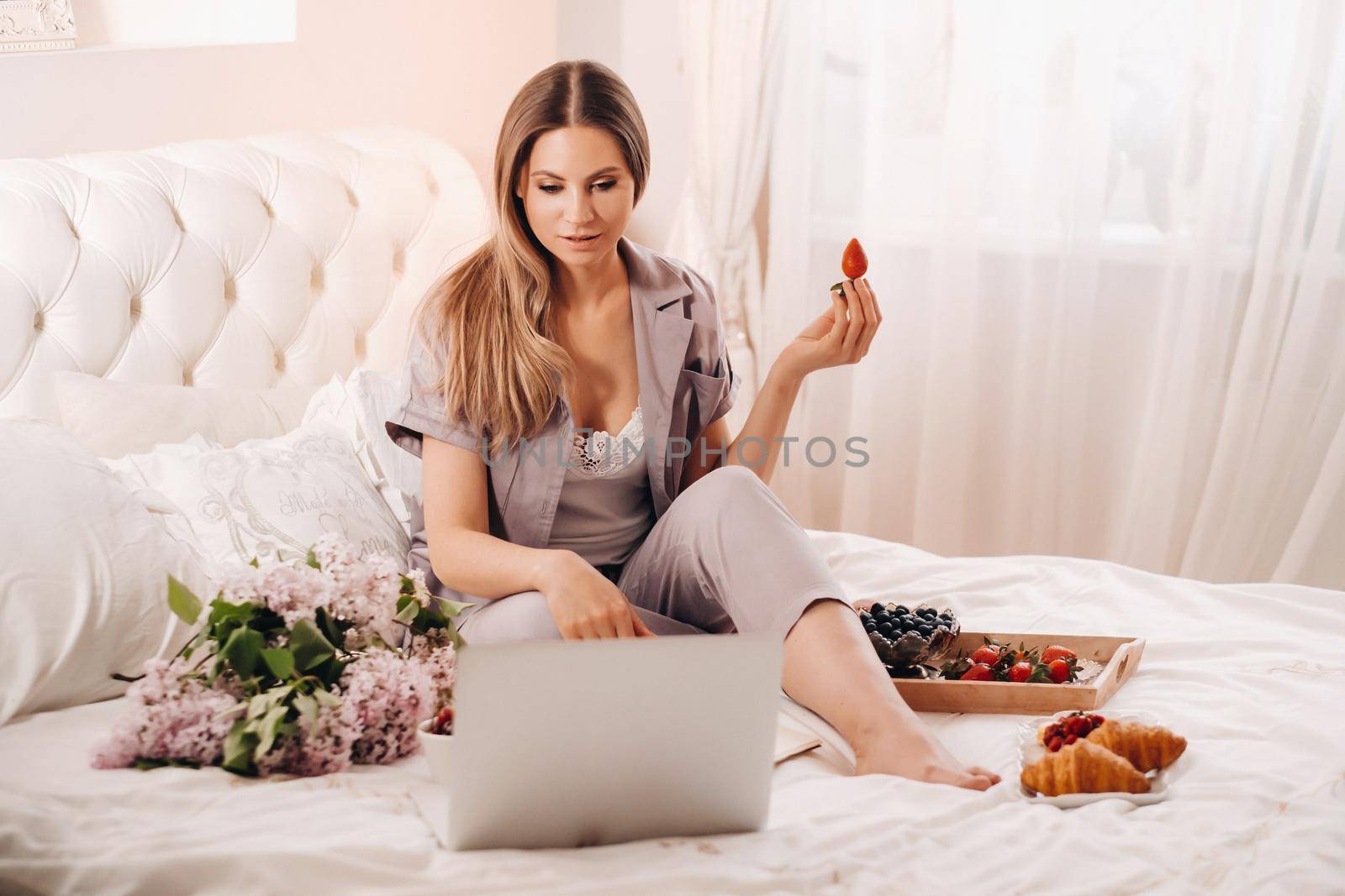 a girl sits in bed in the evening watching a laptop and eating strawberries, a girl in bed eats sweets before going to bed.