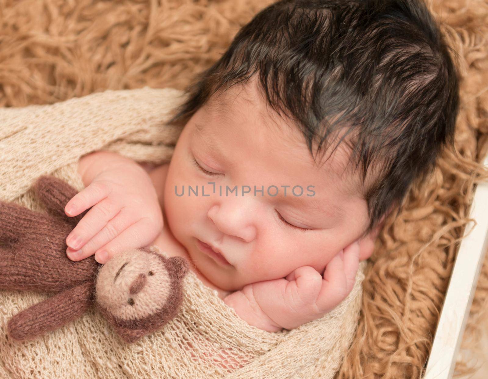 Small black-haired newborn sleeping with a monkey toy on a blanket, closeup