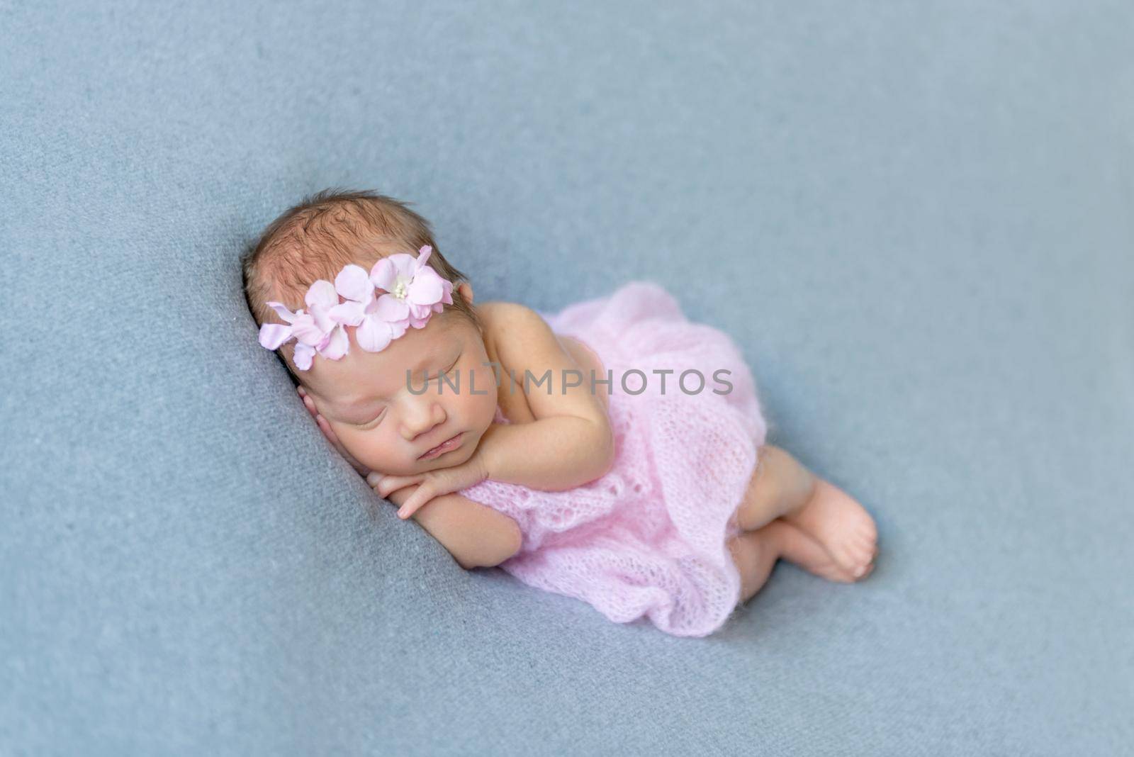 Sweet baby girl sleeping on her tummy, wearing pink little dress, in a flowery hairband