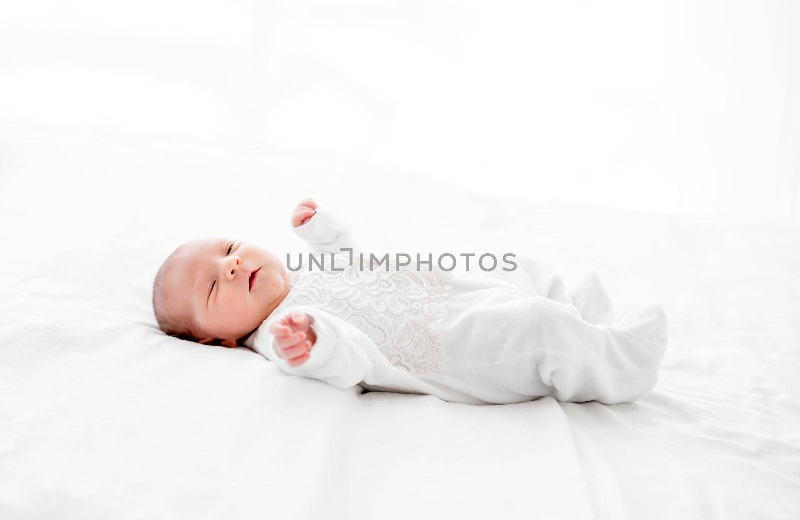 Adorable newborn baby girl wearing white costume lying in the bed and looking at the camera. Cute infant child resting at home