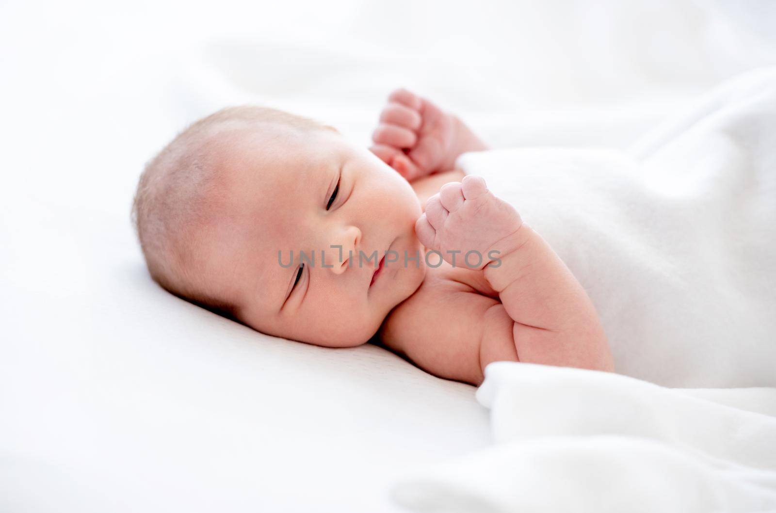 Cute newborn baby girl lying in the bed and sleeping holding her hands close to head. Sweet infant child napping at home