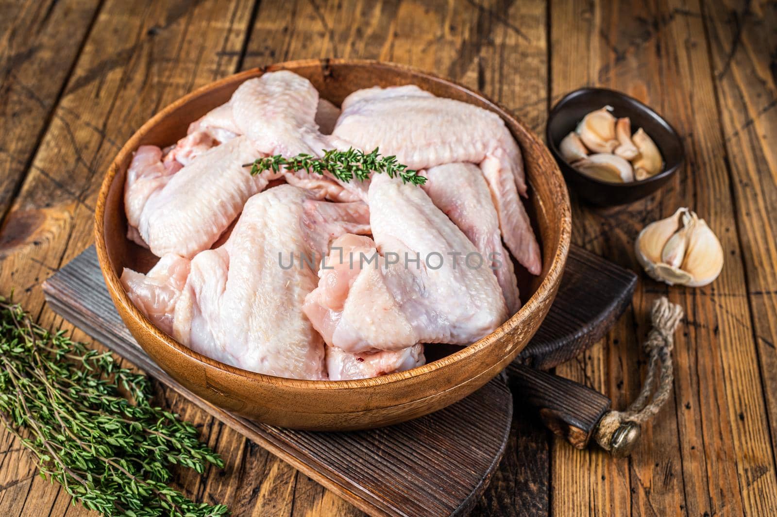 Raw chicken wings in a wooden plate with thyme and garlic. Wooden background. Top view by Composter