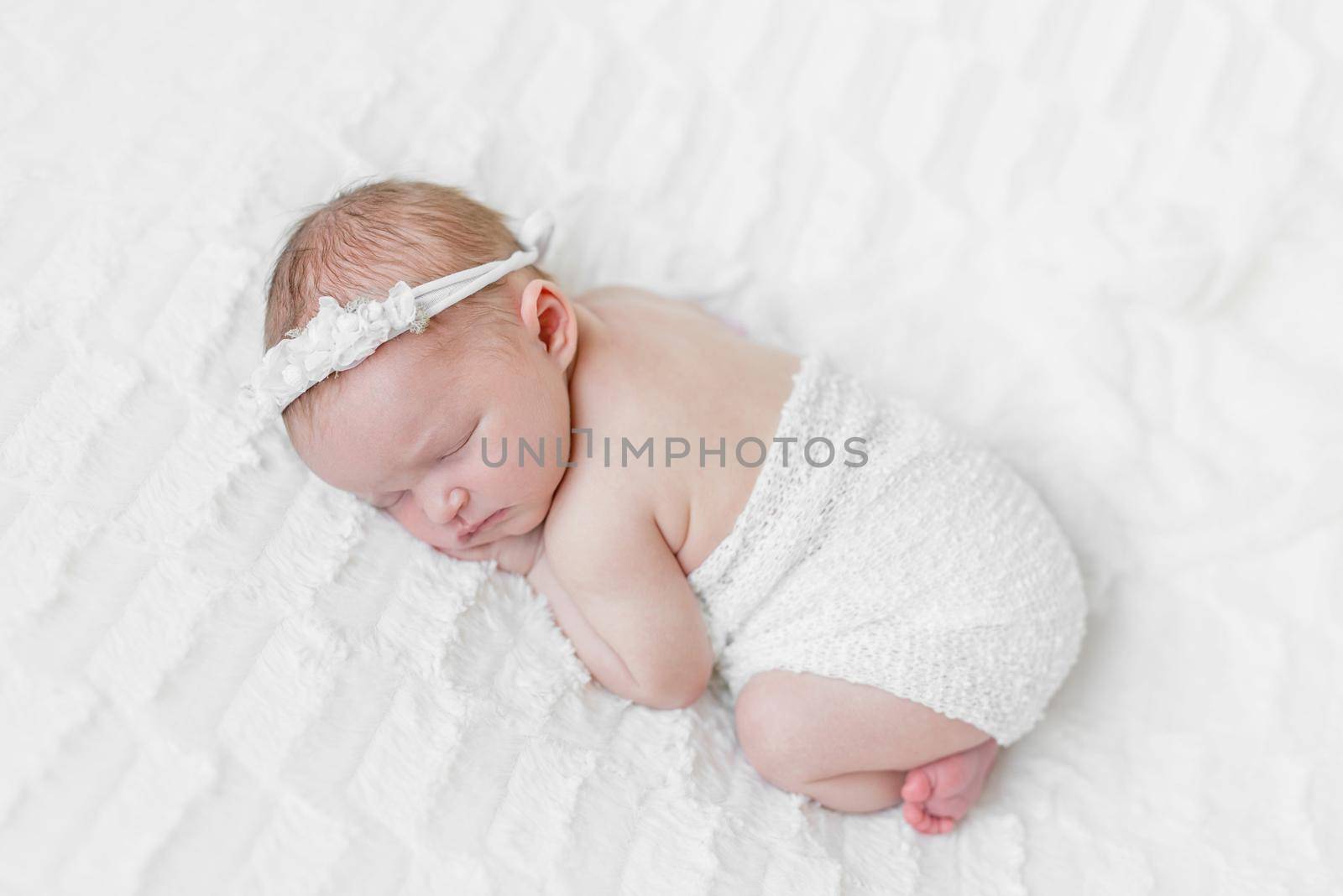Cute baby sleeping on her belly, wrapped up and wearing a flower band