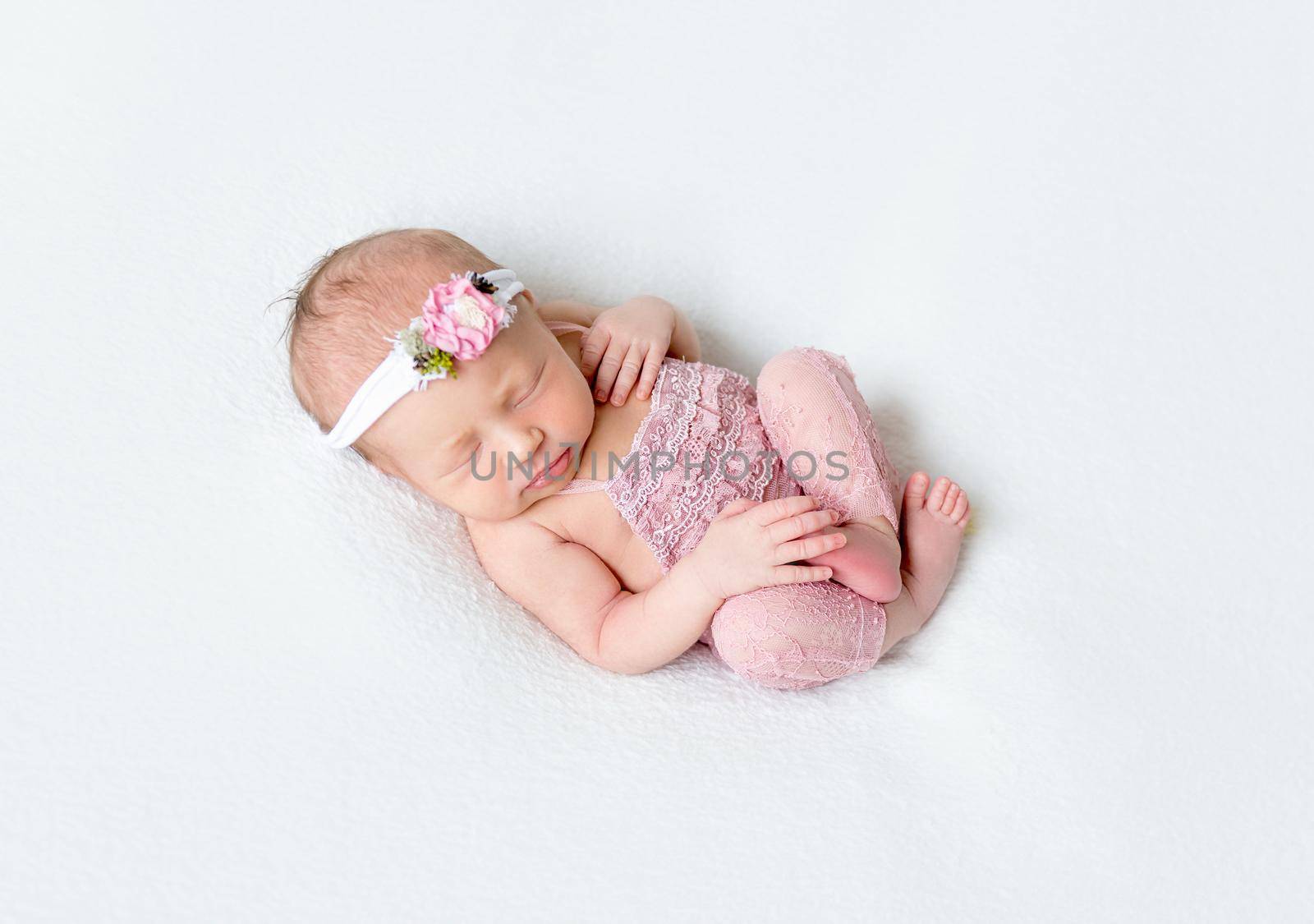 Adorable baby resting in a funny pose, dressed in a pink laced costume