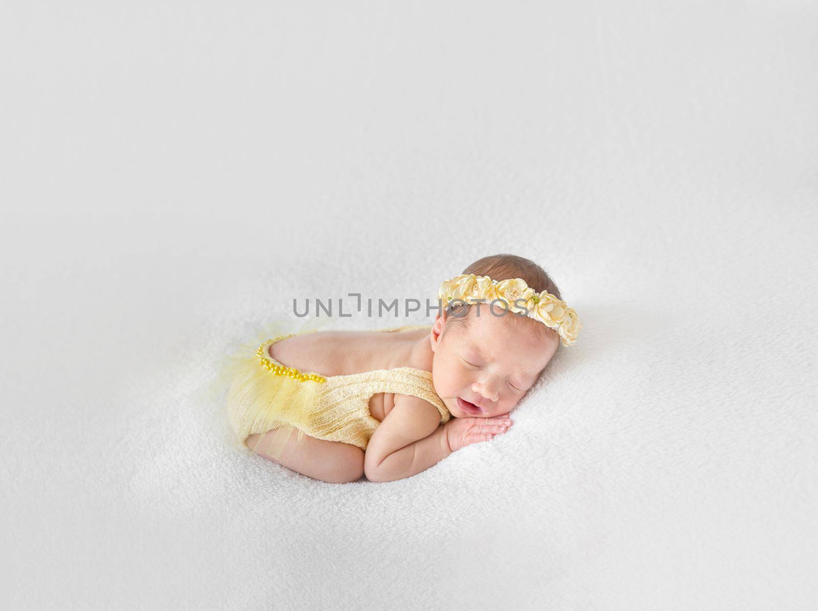 Amazing little kid in a yellow knitted costume napping on her tummy, closeup