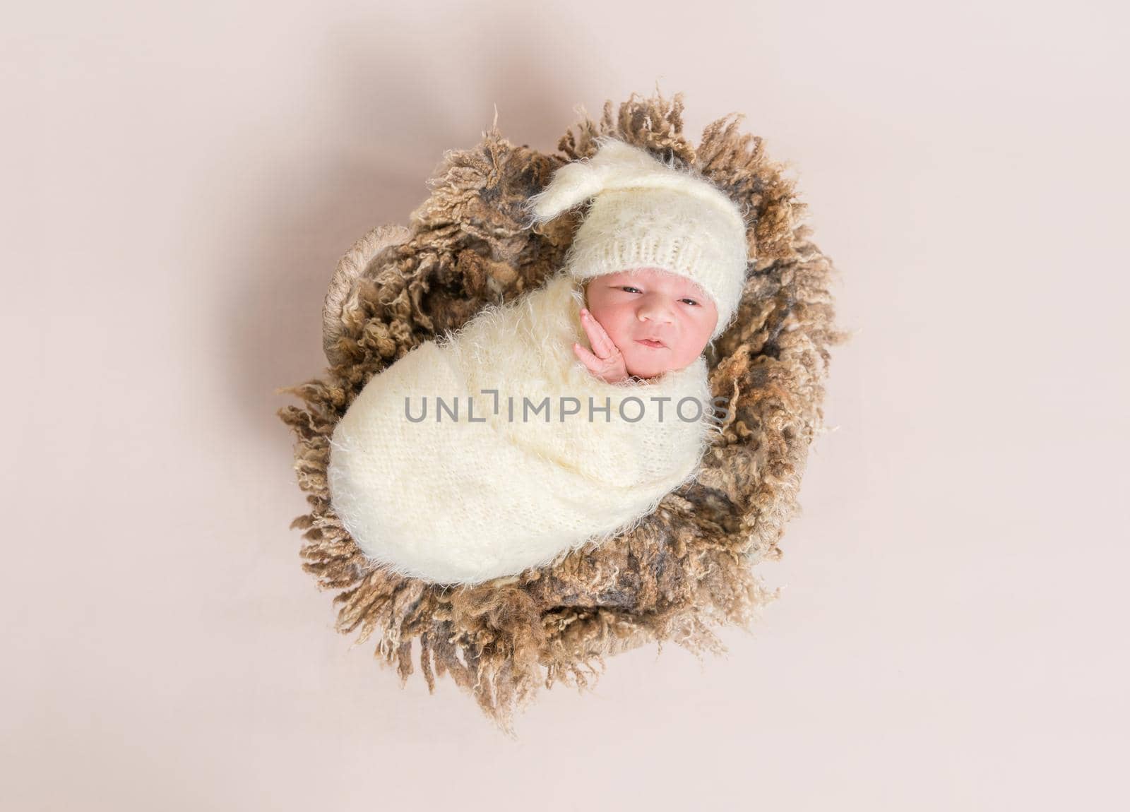 Adorable baby all covered up resting on a big furry brown pillow, topshot
