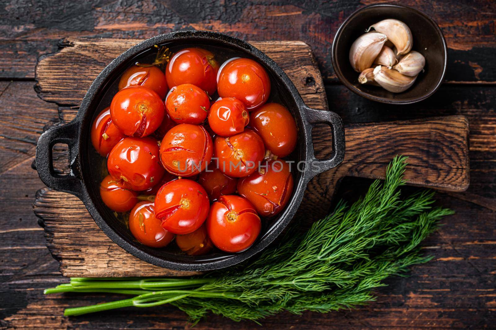 Salted Pickled cherry tomatoes in a pan with herbs and dill. Dark wooden background. Top view.