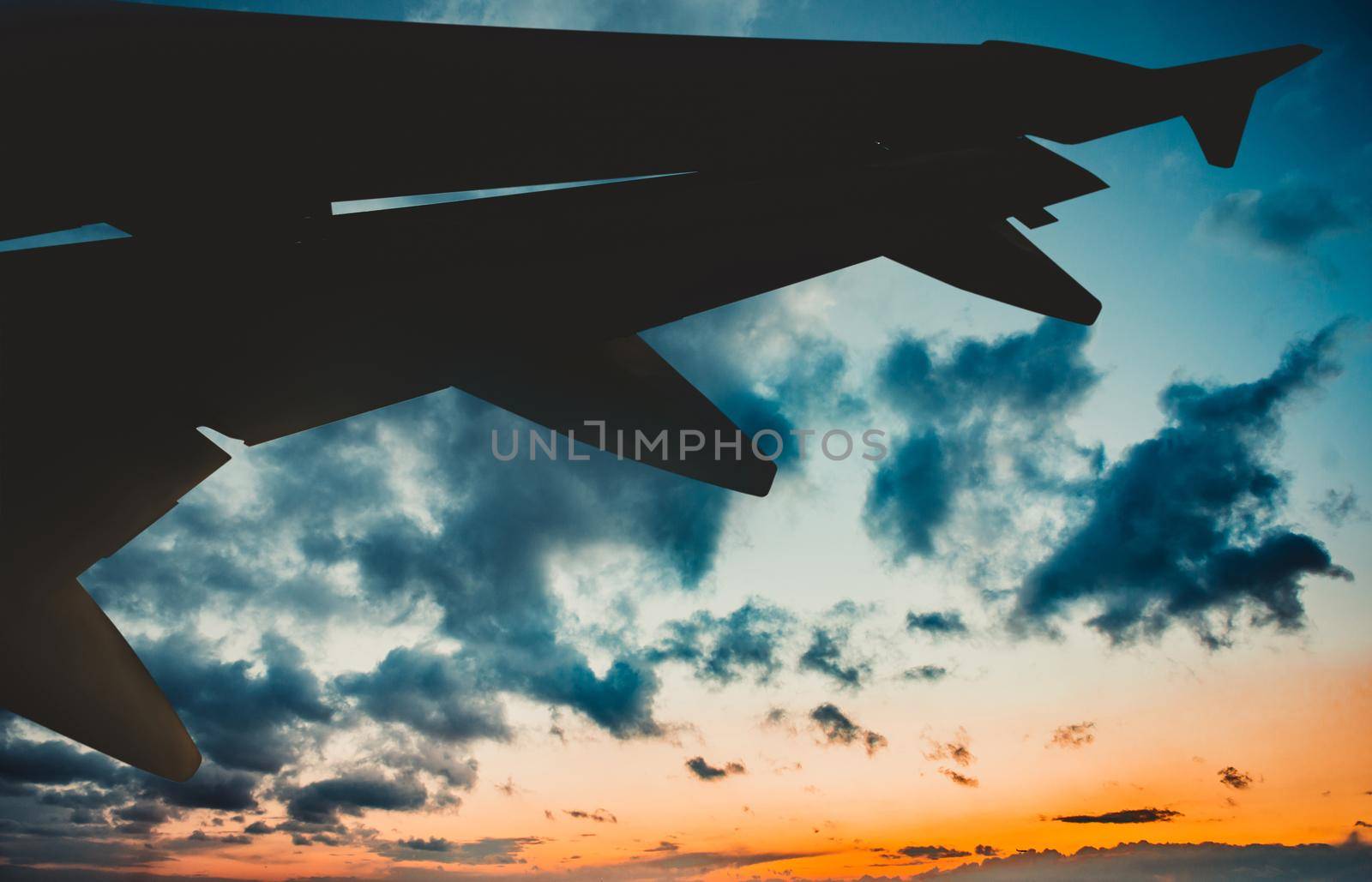 Wing of an airplane flying above the fiery sunset sky