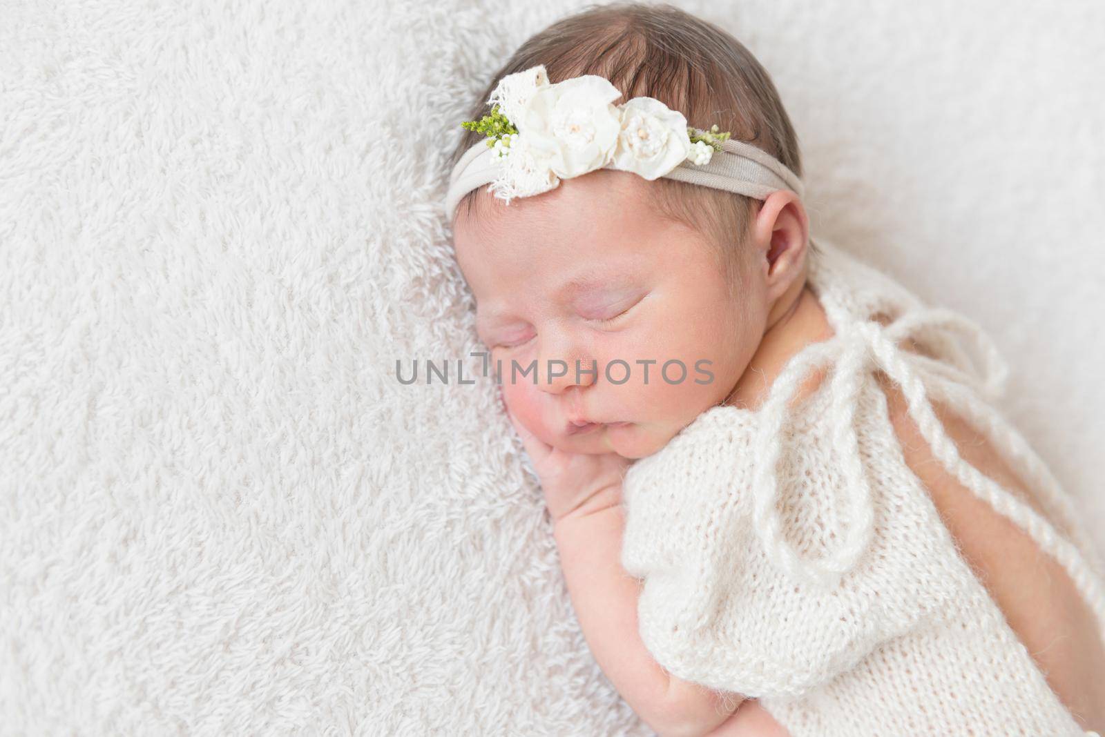 Lovely sleeping baby with a white hairband, dressed in white cute suit napping