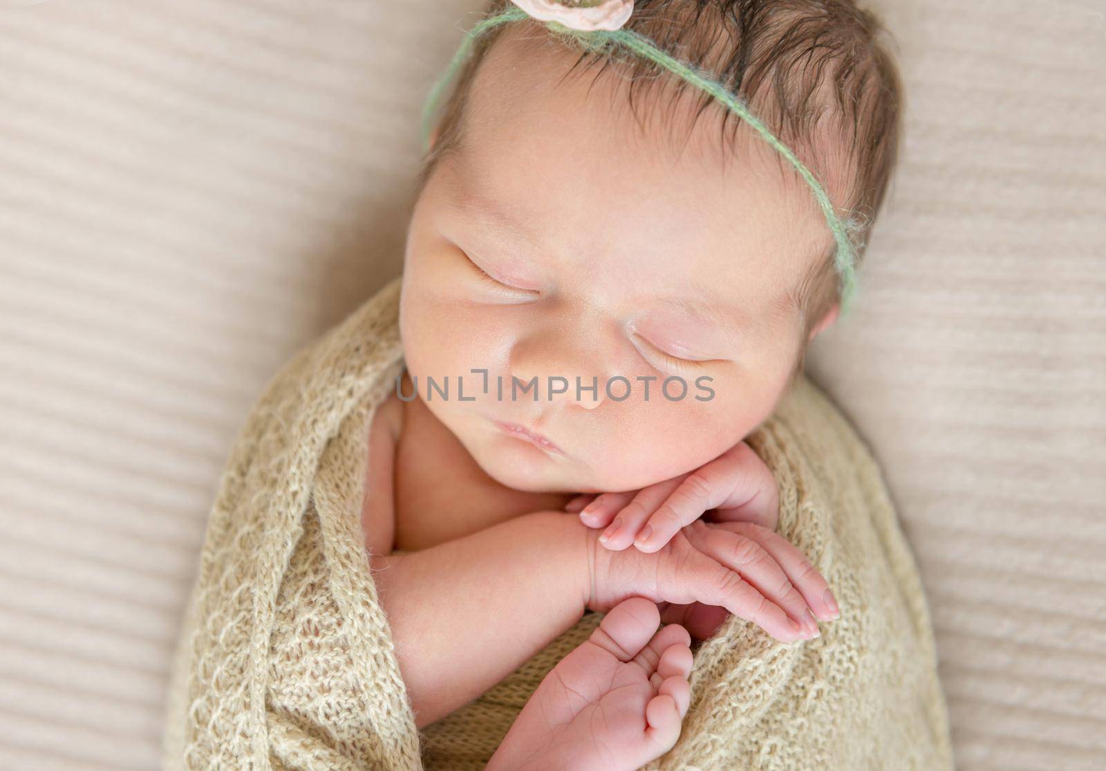 Small child in a flowery hairband sleeping tight covered and wrapped in a scarf, topview