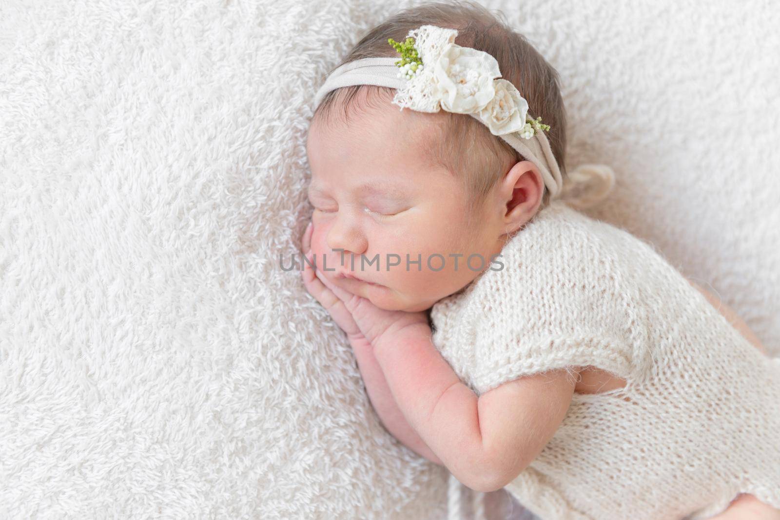 Lovely sleeping baby with a white hairband, dressed in white cute suit napping close-up