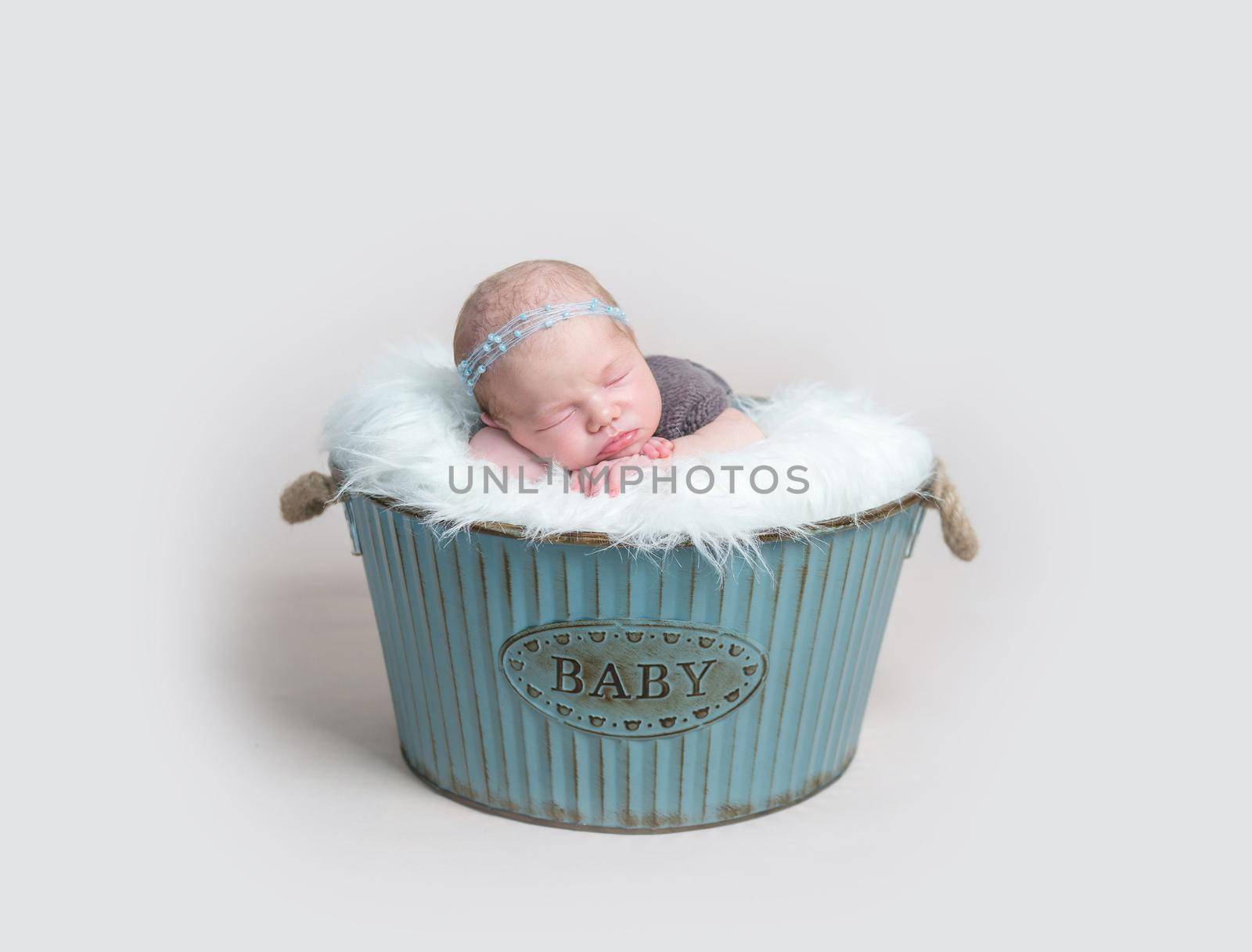 Sweet child napping, dressed in brown knitted suit, in a blue metal basket