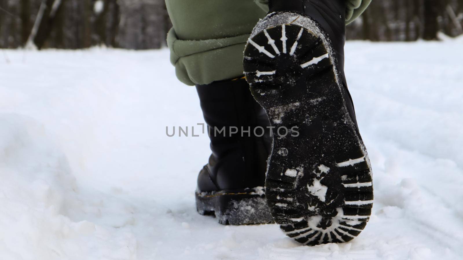 Female legs in black boots, winter walk in the snow. Active woman walking away from the camera in the winter forest. Focus on your legs. Beautiful white winter weather with fresh snowfall