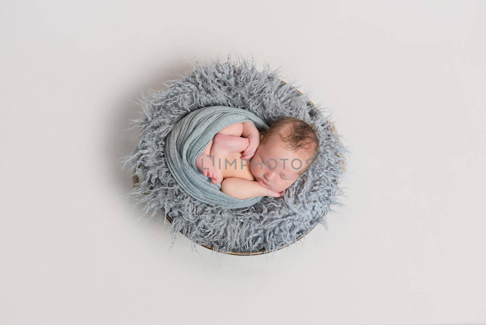 Adorable newborn sleeping curled in his wrap, on soft warm dark gray pillow, topview