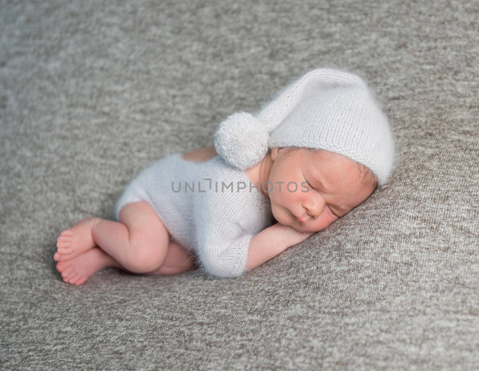 Sweet little baby boy in light blue costume and knitted bonnet with pom pom on grey background.