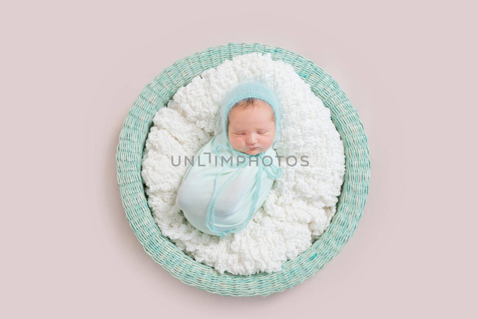 Adorable baby wrapped in blue blanket sleeping on white and blue bedding, in basket, topview