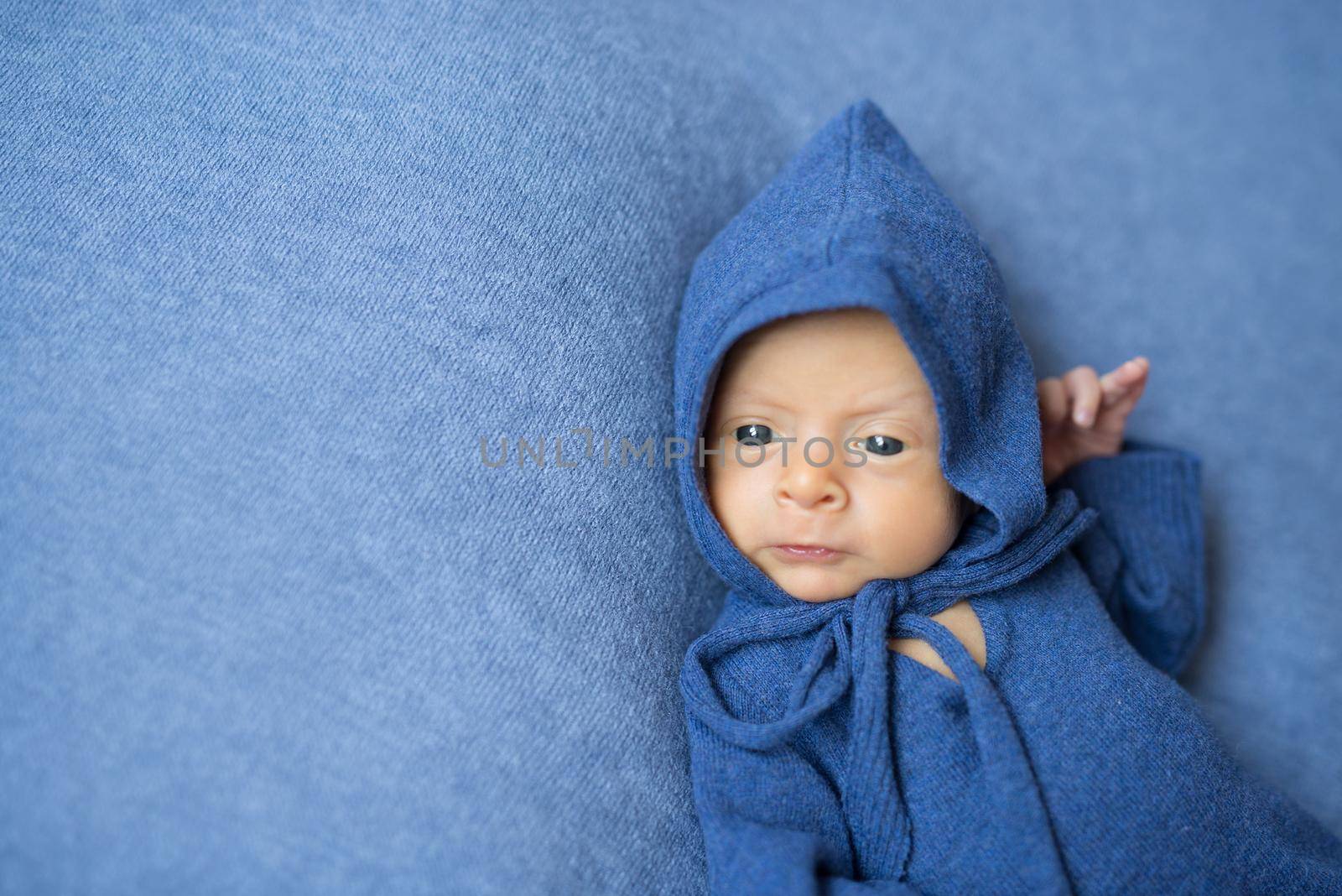 little newborn baby in blue jumpsuit with hood on his head lying on blanket