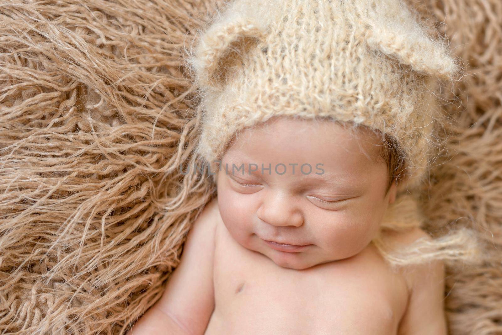 asleep smiling newborn baby in knitted hat on furry blanket, close up